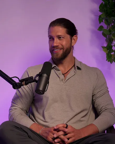 Kevin Cox with a soft smile in a podcast studio, in a grey shirt beside a microphone.