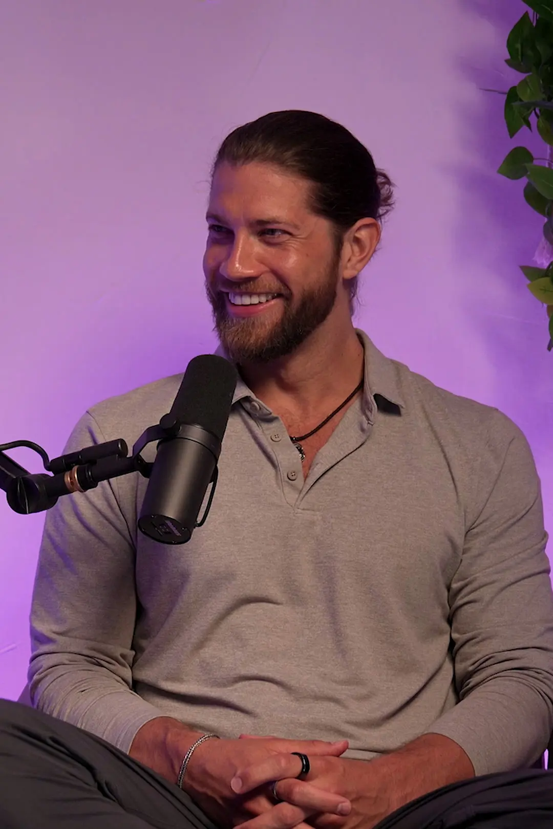 Kevin Cox smiling in a podcast studio, in a grey shirt beside a microphone, looking toward the host.