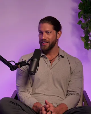 Kevin Cox in a podcast studio, listening with a gentle smile, in a grey shirt.